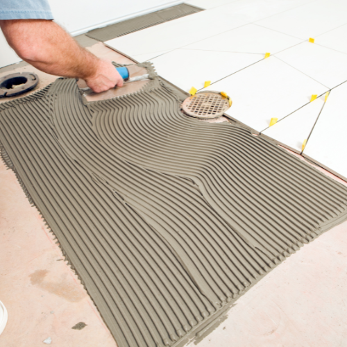 contractor-applying-thin-set-mortar-with-a-notched-trowel-for-floor-tile-installation-around-a-drain - Fix It-Cincy contractor-applying-thin-set-mortar-with-a-notched-trowel-for-floor-tile-installation-around-a-drain